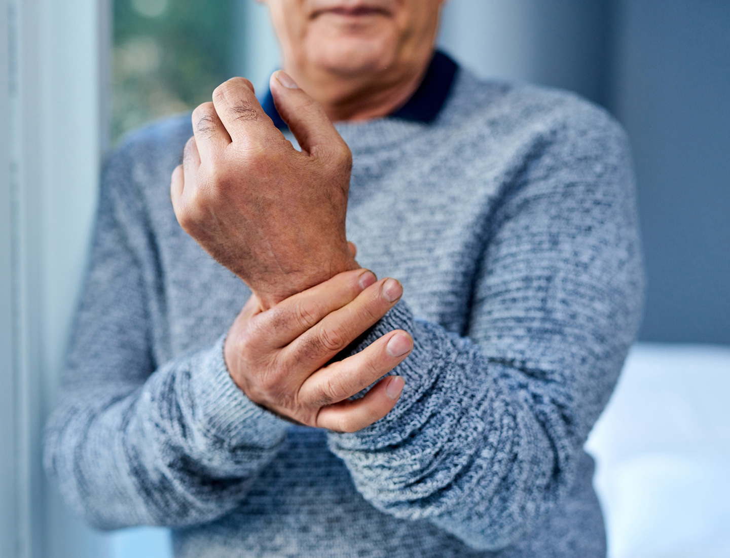 Close-up photo of an older adult holding their wrist in their other hand.