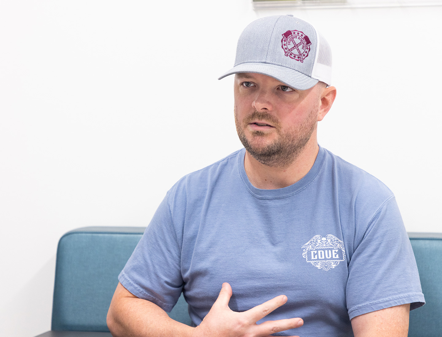 Tyler Cronin seated in an blue bench wearing a blue t-shirt and gray baseball cap.