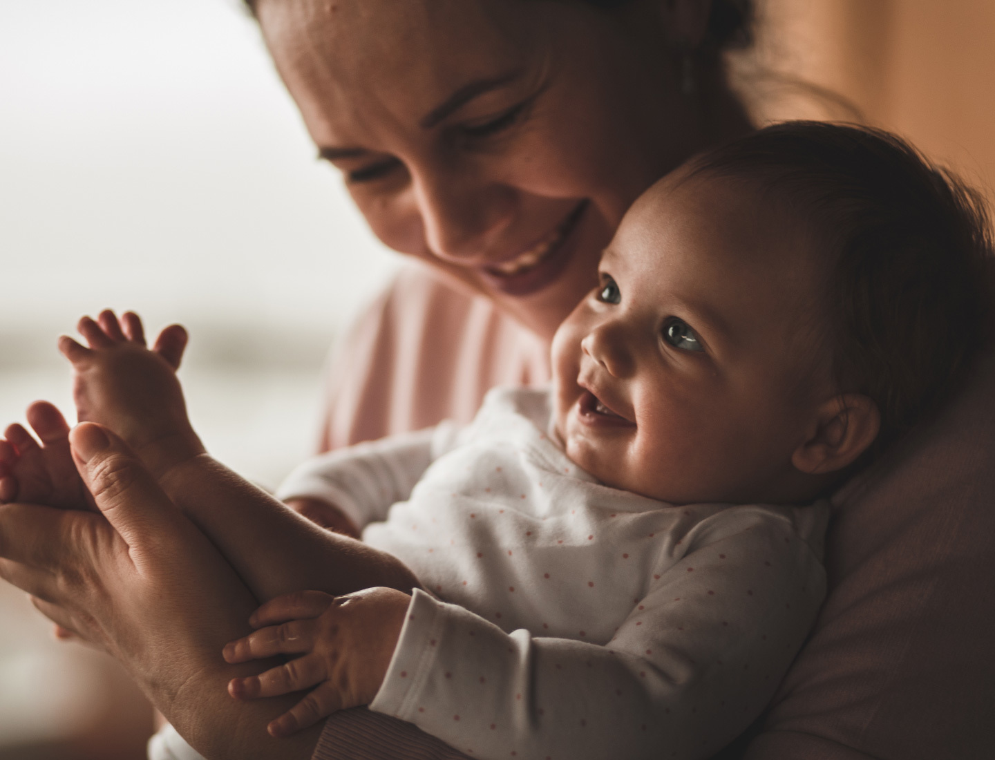 A mother holds her smiling baby in her arms.