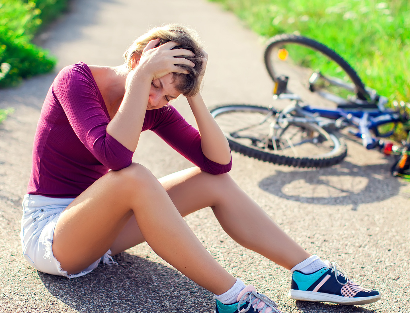 A young person who has fallen off their bike cradles their head in their hands.