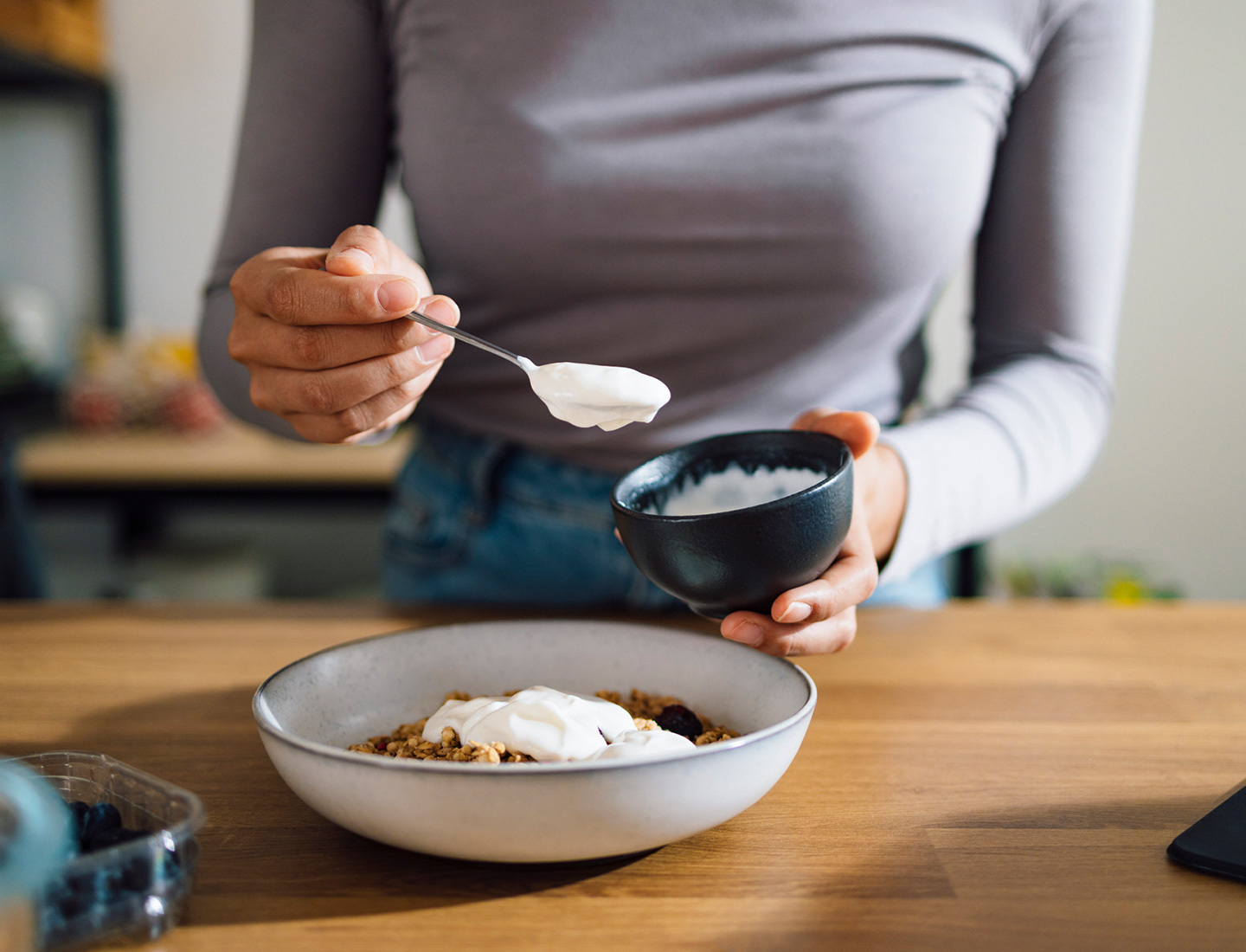 Close-up of a woman's hands as she scoops yogurt onto a bowl of granola.