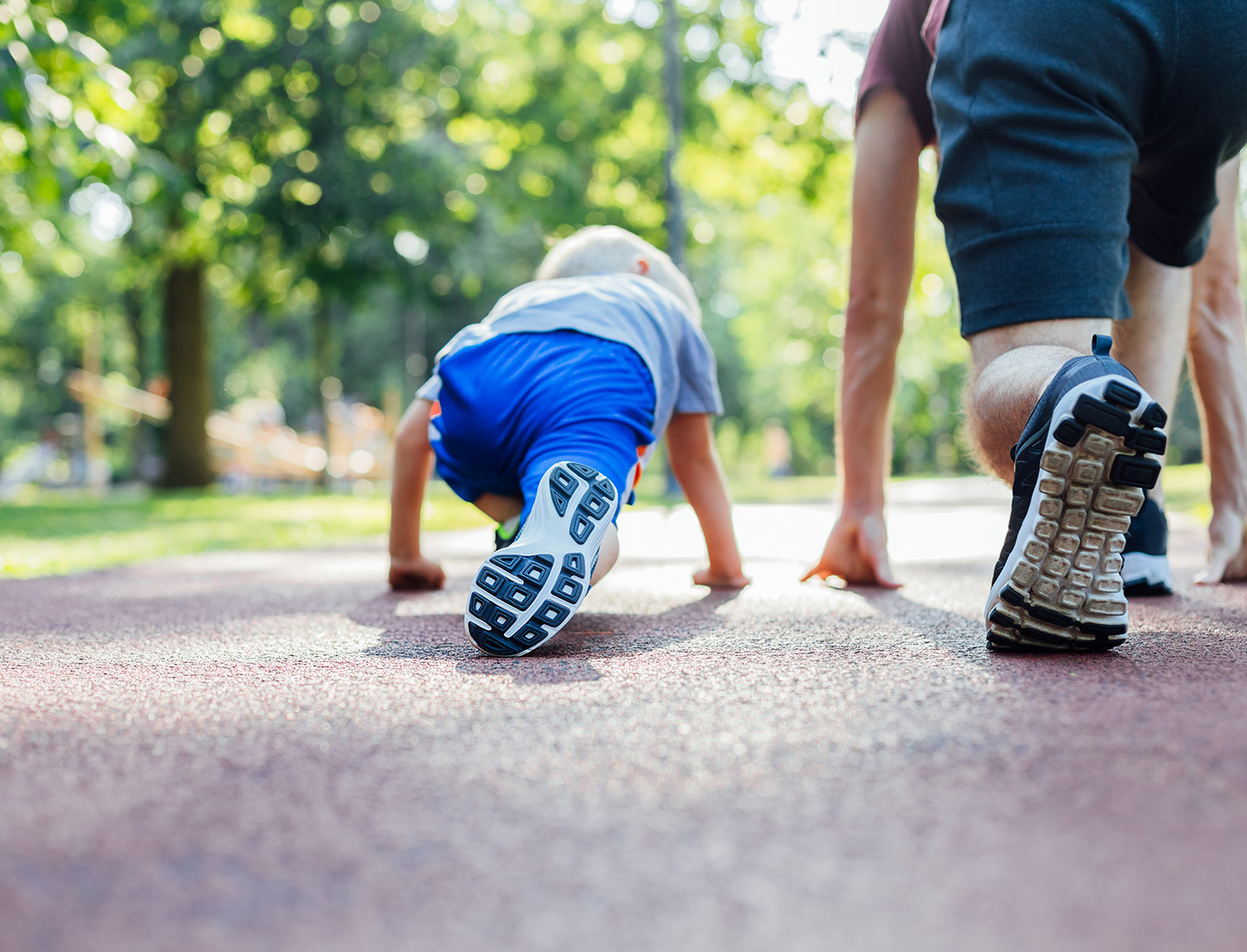 A young child squats on the ground in a runner's starting stance. Next to him, in the same position, is his father.