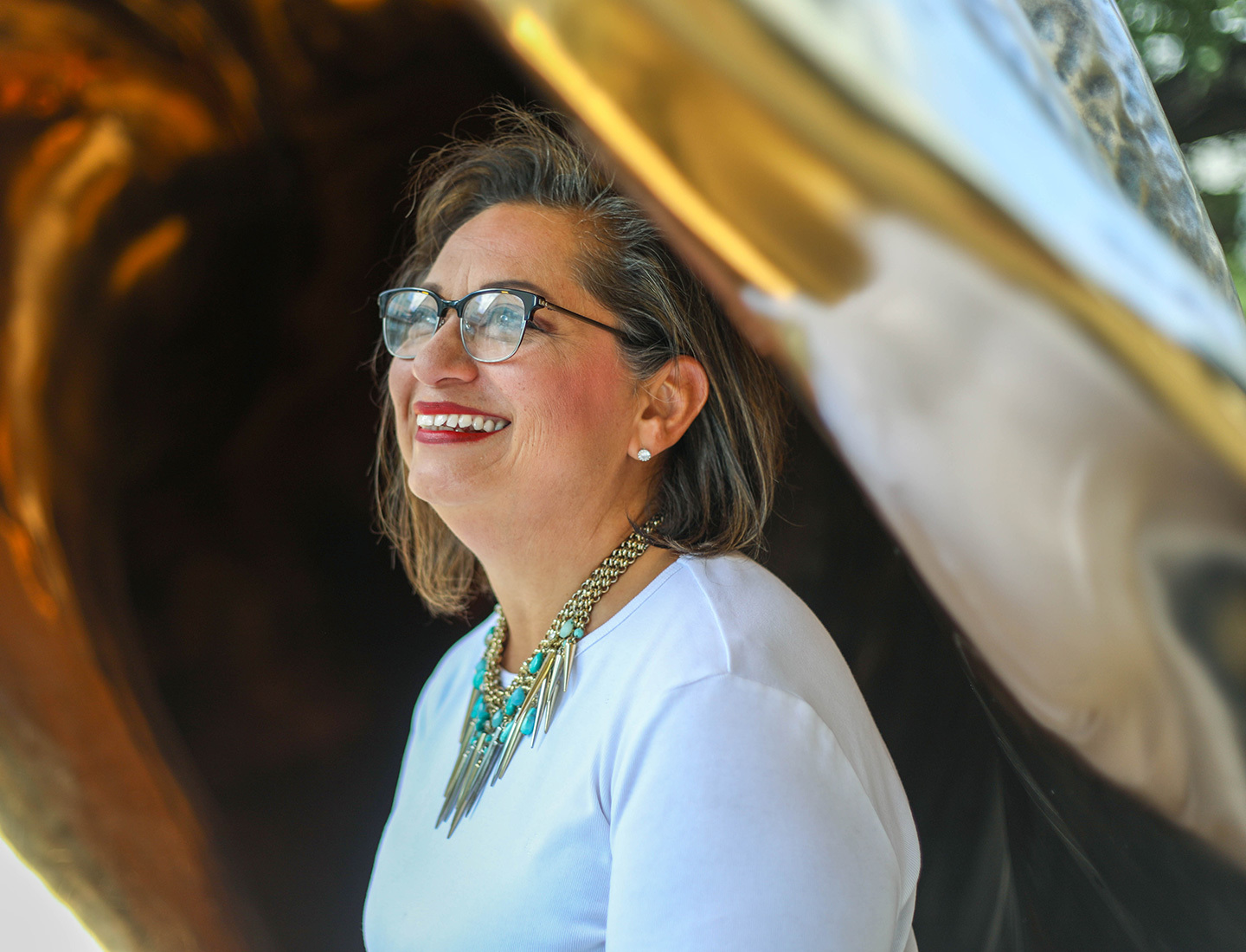 Kat, who works as a senior administrator for facilities at the Dell Medical School, stands smiling near the large seashell sculpture displayed in the medical plaza.