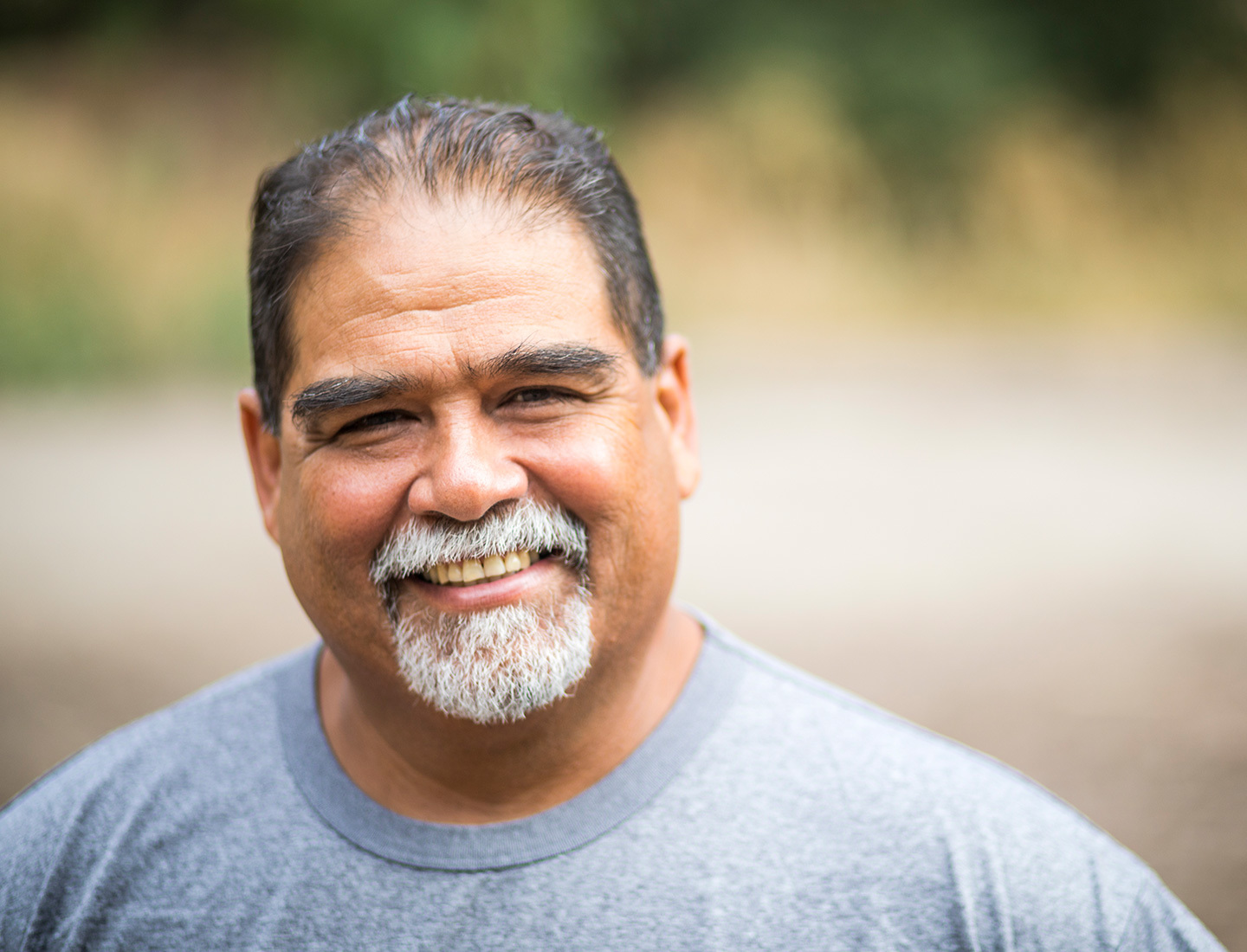 A middle-aged Latinx man with a white mustache and goatee smiles at the camera.