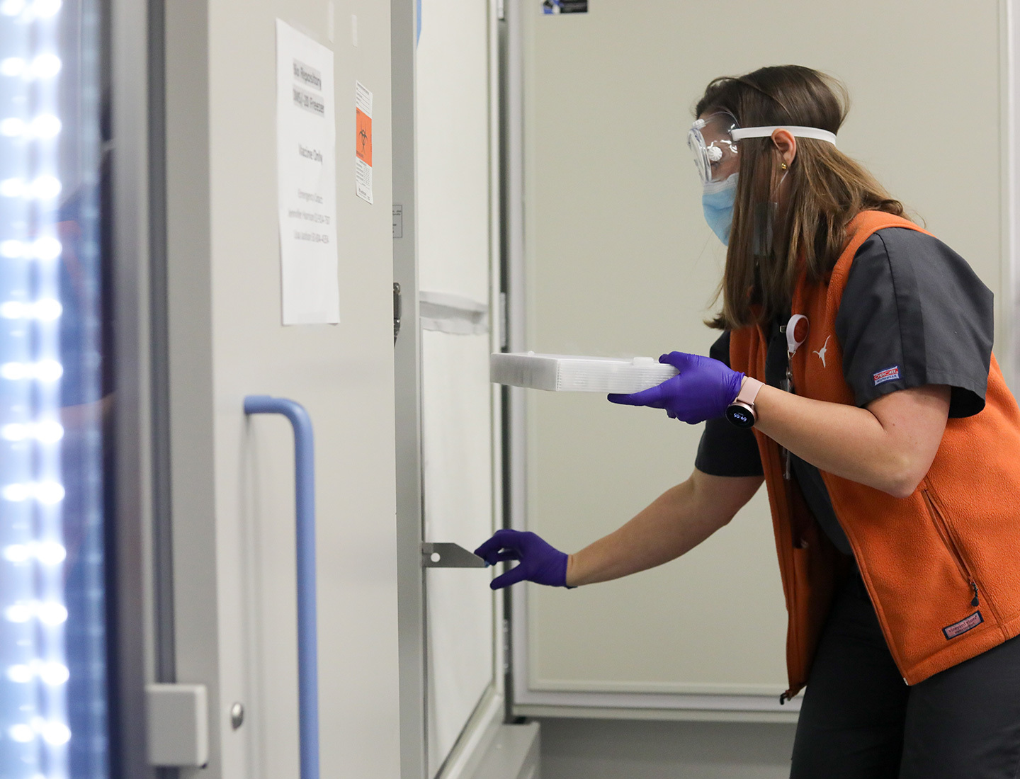 The first tray of COVID-19 vaccine is held by a clinician, in protective gloves, mask and goggles, getting ready to open the sub zero freezer for storage.