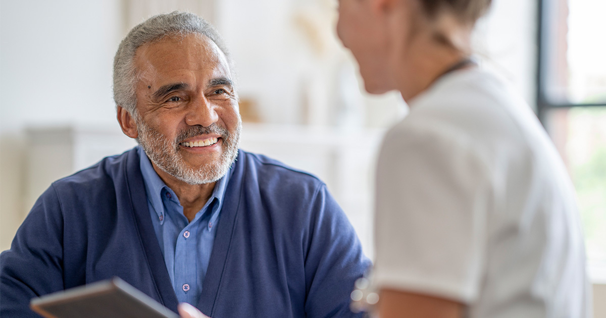 Smiling older adult man speaks with a healthcare professional during a consultation in a bright office.