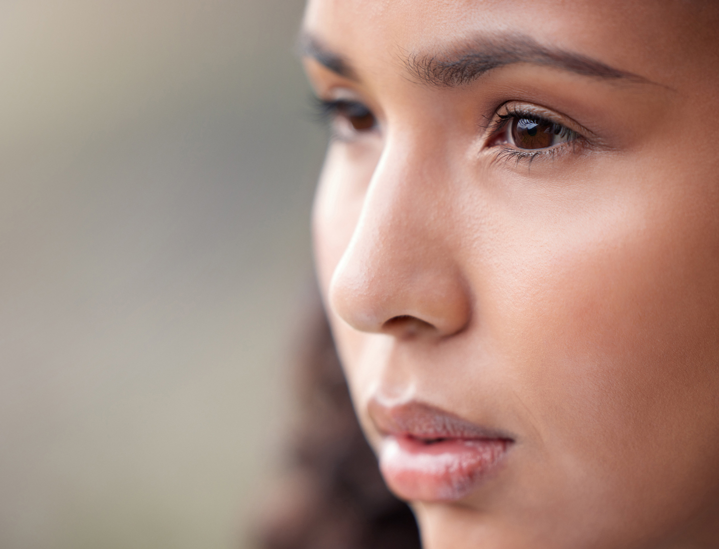 A young woman with brown eyes looks off in the distance with a blurry background behind her.