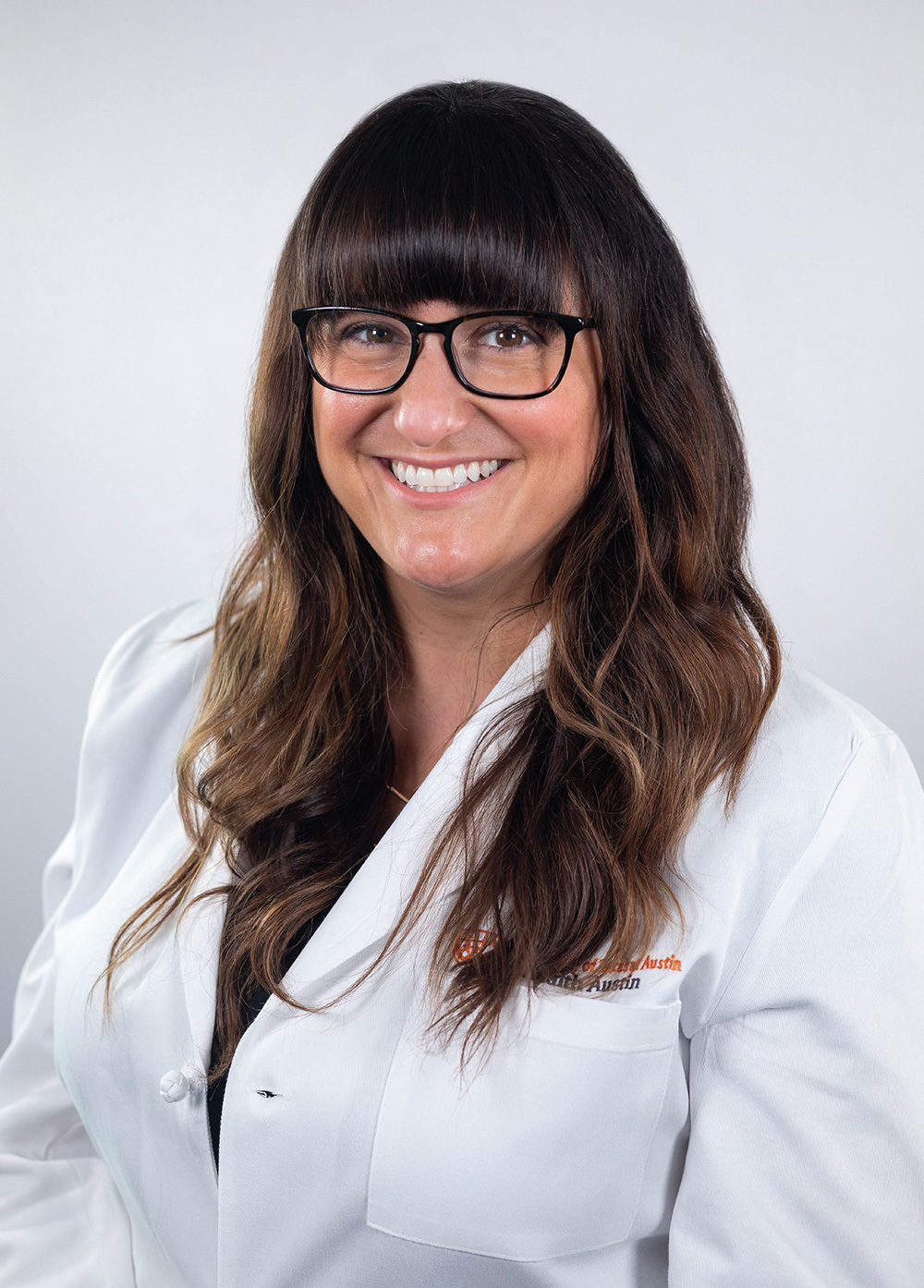 Pediatric neuropsychologist Amanda Winter-Greenberg, PhD, ABPP, wearing a white coat and smiling in front of a white backdrop.