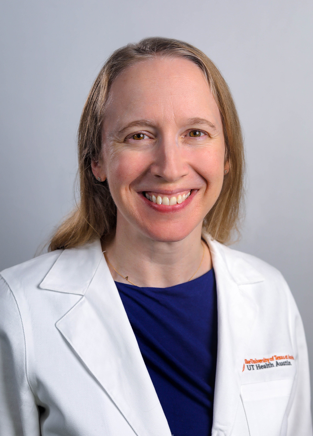 Pediatric neurology Audrey Brumback, MD, PhD, wearing a white coat and smiling in front of a white backdrop.