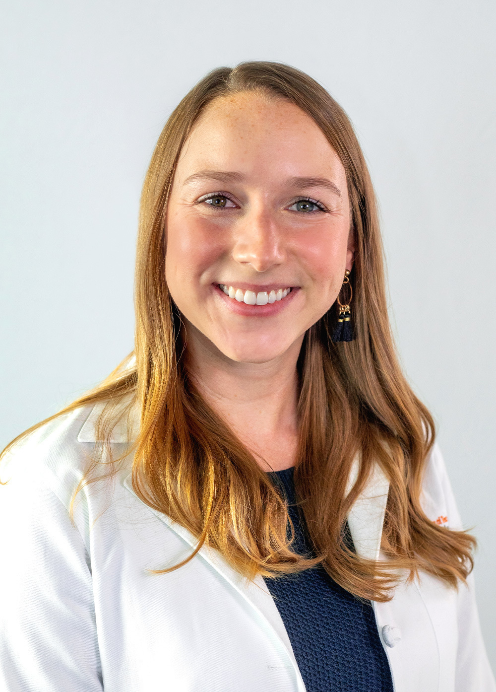 Pediatric nurse practitioner Chelsea White, MSN, APRN, CPNP-PC, wearing a white coat and smiling in front of a white backdrop.