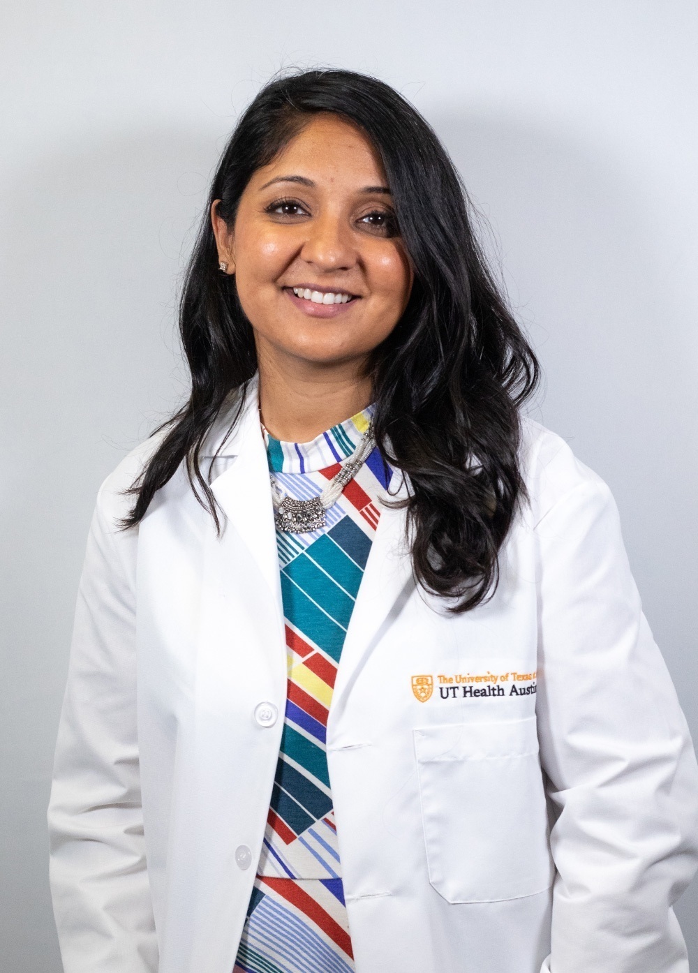 Pediatric psychologist Puja G. Patel, PhD, wearing a white coat and smiling in front of a white backdrop.