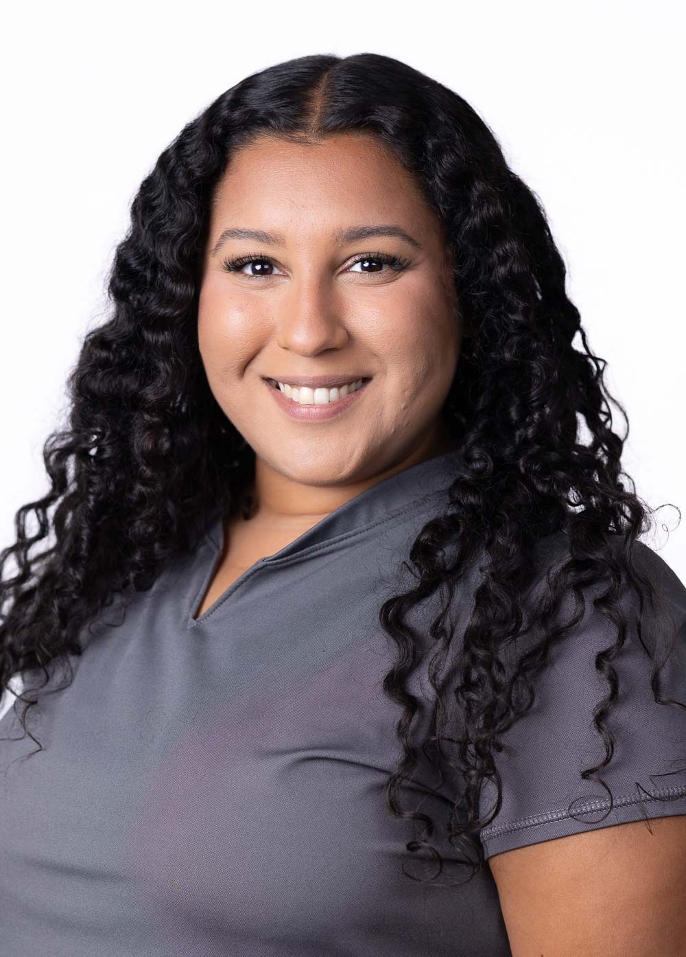 Alexys Campos is smiling and looking at the camera. She is wearing dark grey scrubs.