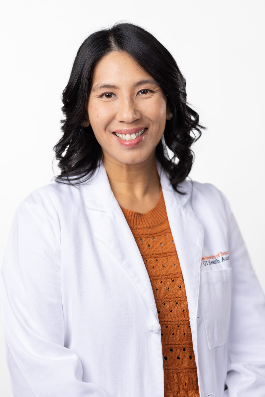 Brenda Chang is smiling at the camera. She is wearing a white coat and a burnt orange sweater.