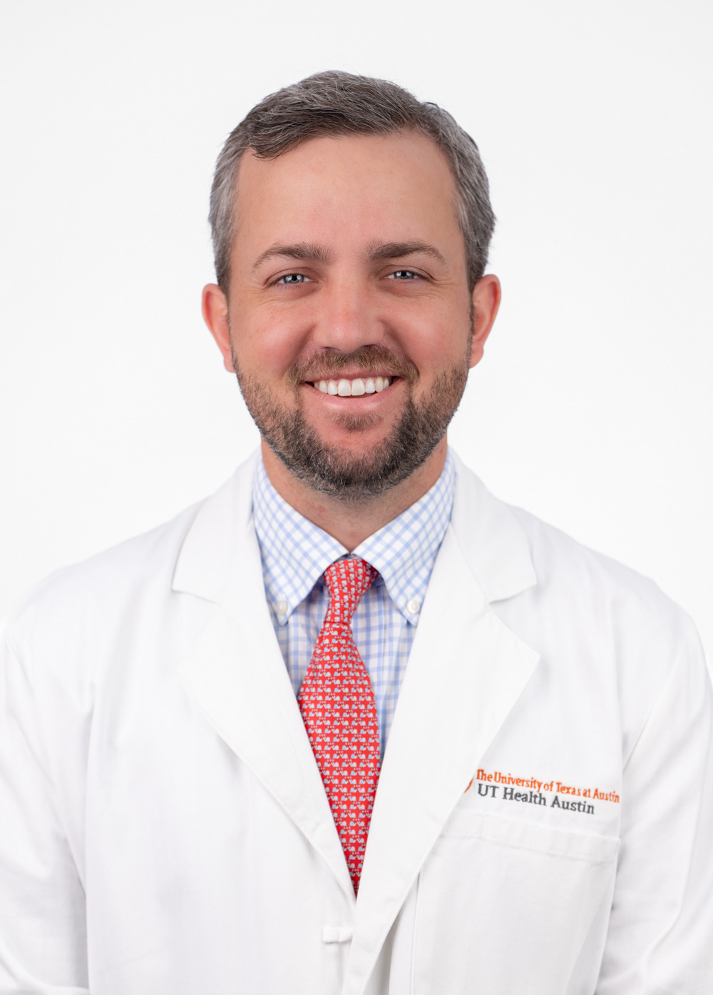 Dr. Charles Fraser III is wearing a white coat , blue collared shirt, and a red tie. He is smiling at the camera.