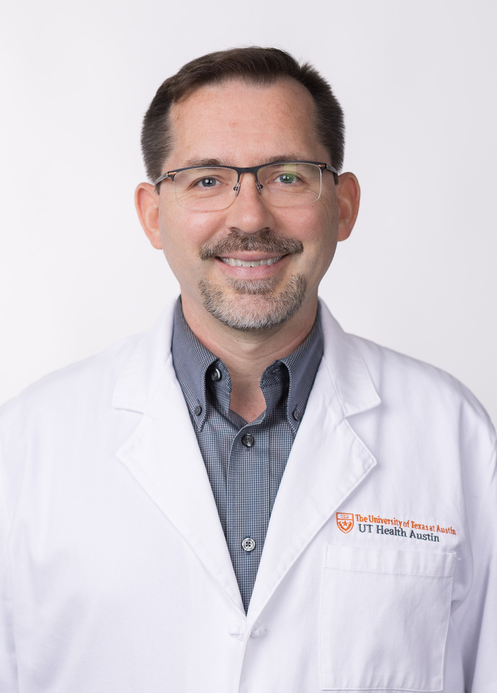 Dr. Jon Willie is smiling at the camera. He is wearing glasses, a white coat, and a navy dress shirt.