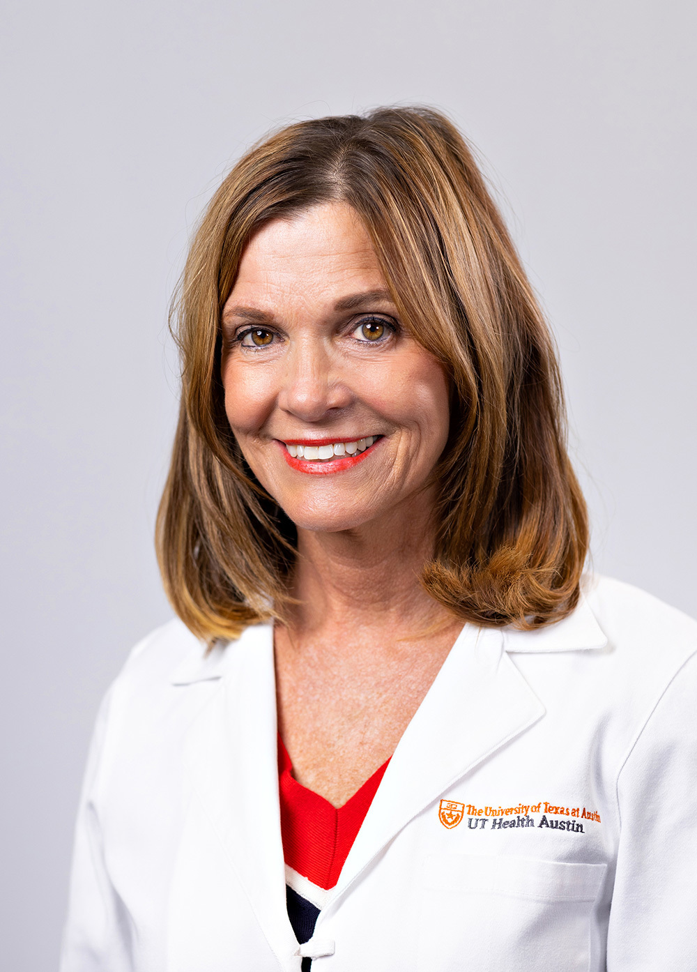 Acute care pediatric nurse practitioner Joni Zauhar, MSN, ARNP, CPNP-AC/PC, FNP wearing a white coat and smiling in front of a white backdrop.