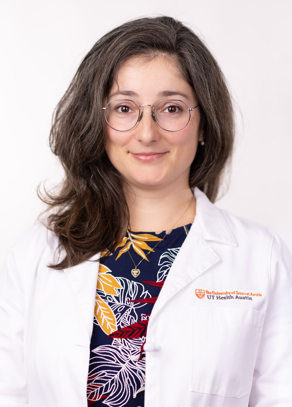 Dr. Kristina Tzartzeva is smiling and wearing a white coat with a floral print dress.