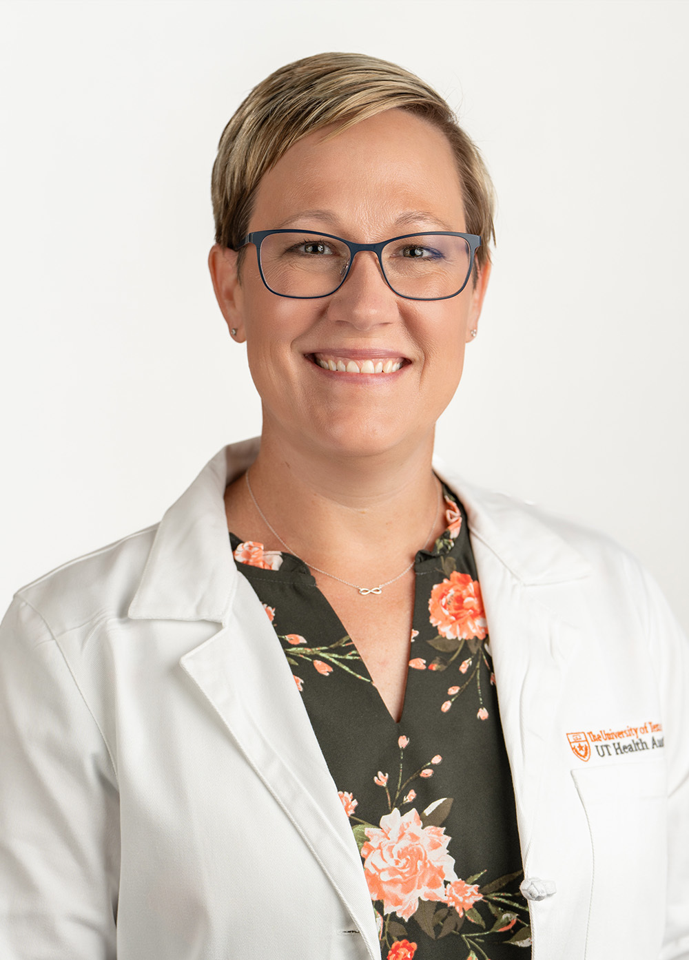 Nurse practitioner Mackenzie J. Field, MSN, APRN, AGACNP-BC smiling in front of a white backdrop. She is wearing a white coat with an embroidered UT Health Austin logo.