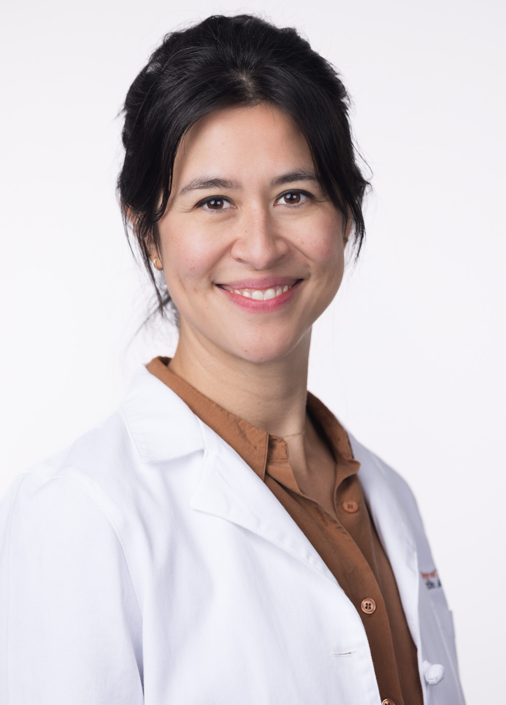 Dr. Meagan Williams is looking at the camera and smiling. She is wearing a white coat and a brown collared blouse.
