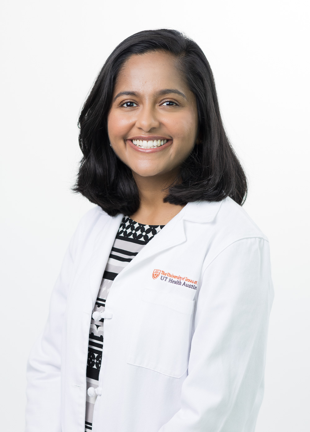 Nimmy Thomas is smiling at the camera. She is wearing a white coat and a black and white patterned blouse.