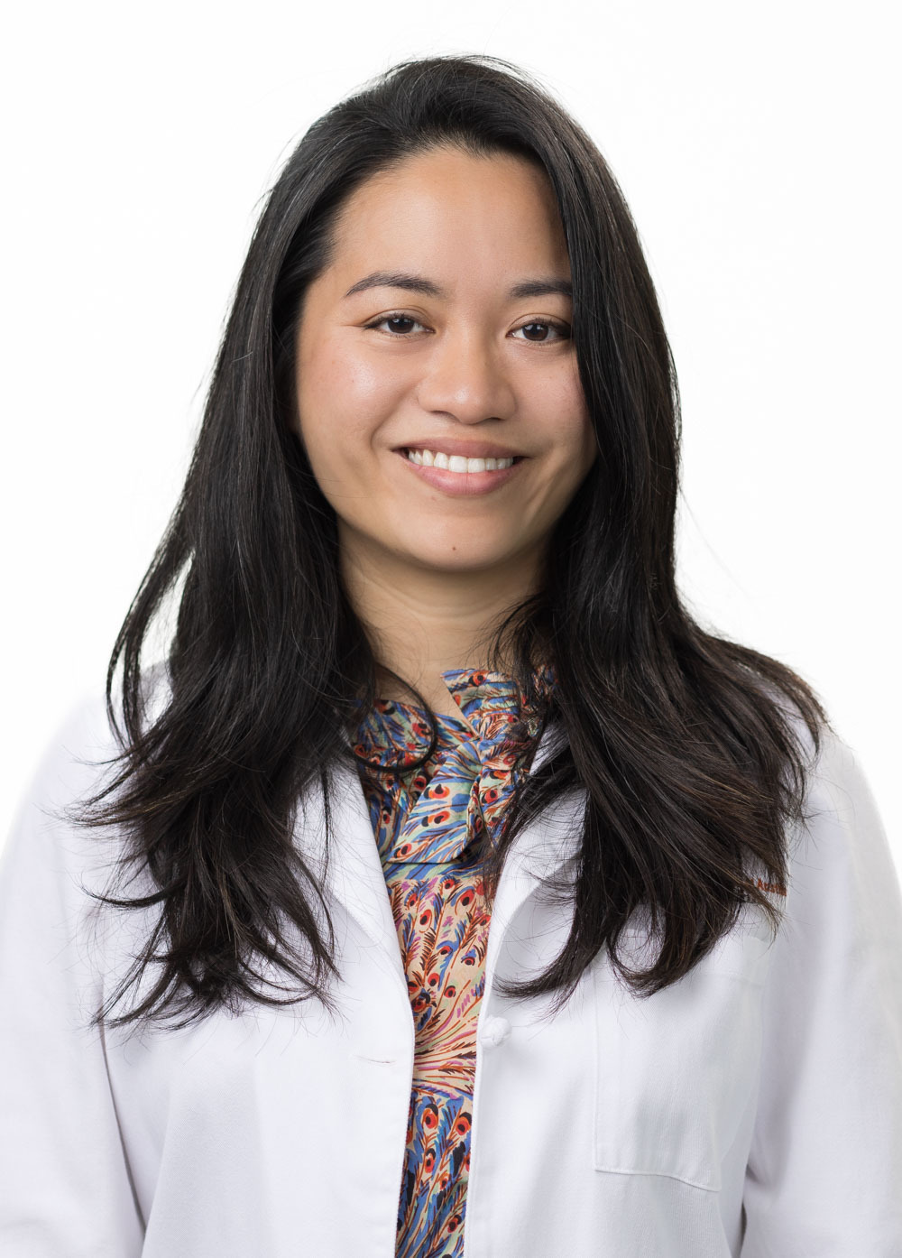 Sharyl Wee is looking at the camera and smiling. She is wearing a white coat and a multicolored blouse.