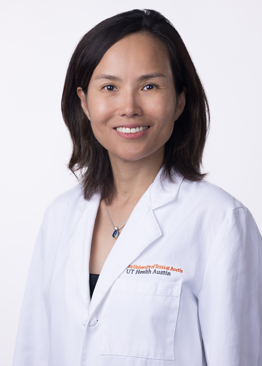 Dr. Li is smiling at the camera. She is wearing a white coat and a black blouse