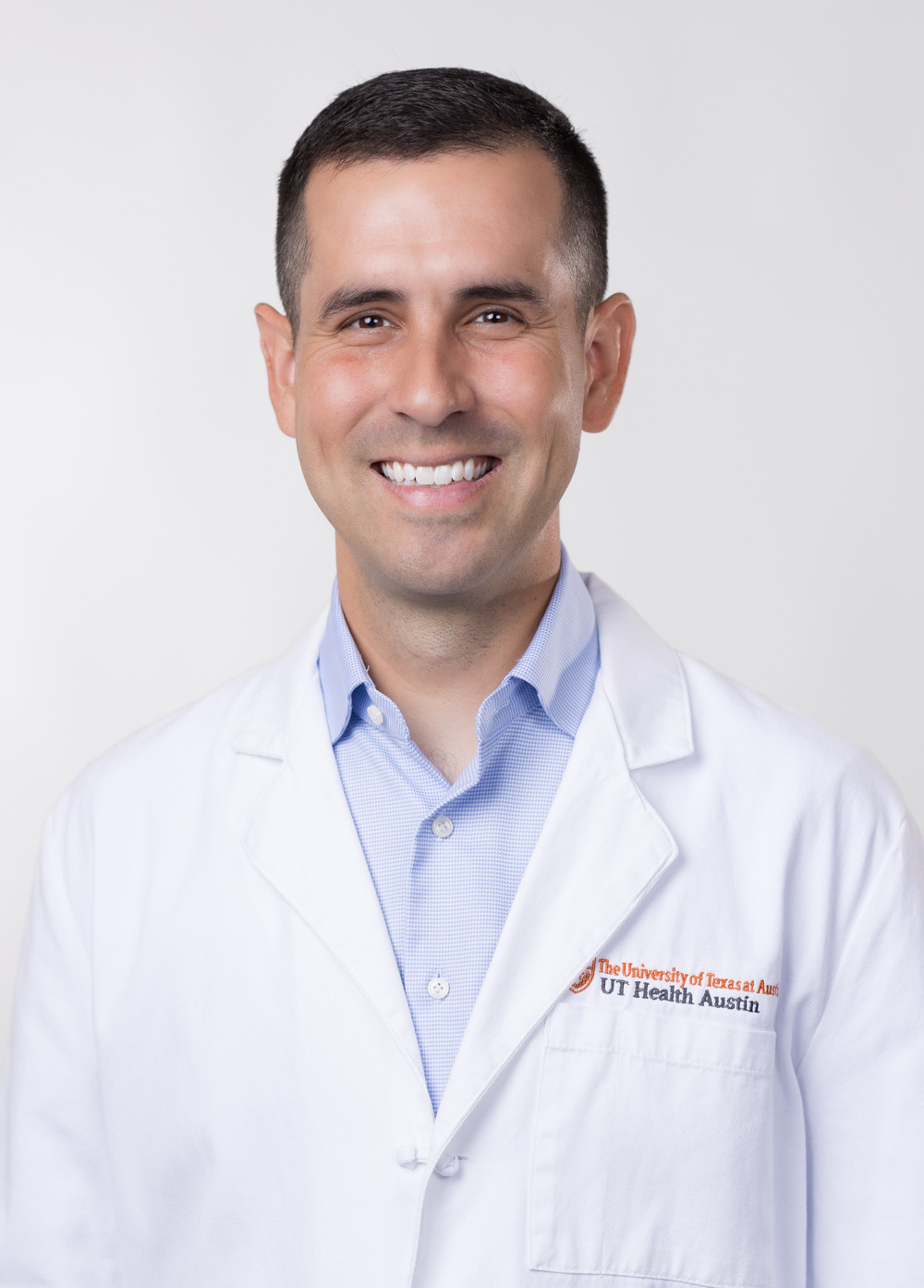 Dr. Sullivan Ayuso is smiling at the camera. He is wearing a white coat with a light blue dress shirts.